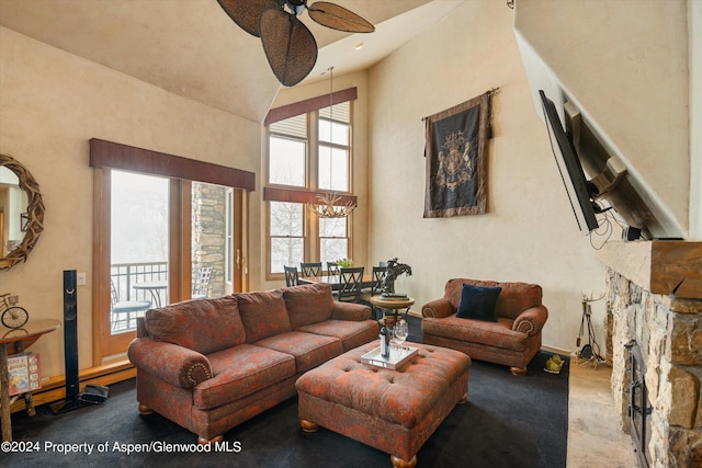 living room featuring a stone fireplace, a towering ceiling, and ceiling fan with notable chandelier