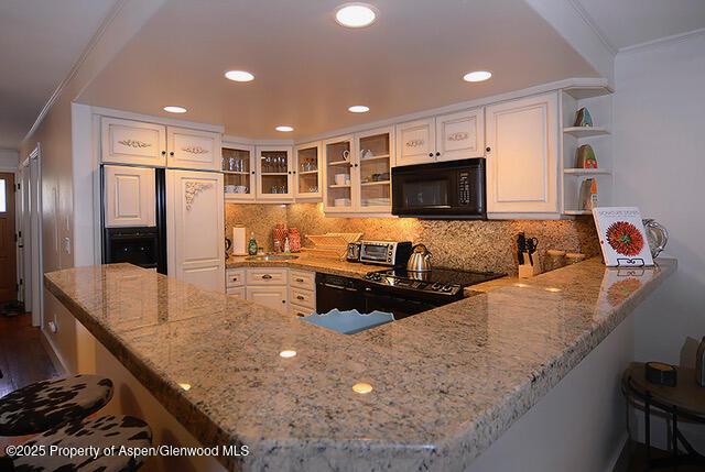 800 E Hopkins Ave Unit A-1, Aspen, CO 81611 - kitchen with black appliances, light stone counters, ornamental molding, a kitchen breakfast bar, and a peninsula