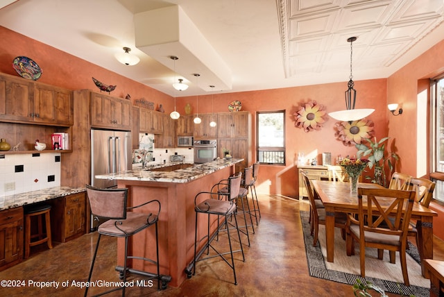 kitchen featuring decorative backsplash, light stone counters, hanging light fixtures, and appliances with stainless steel finishes