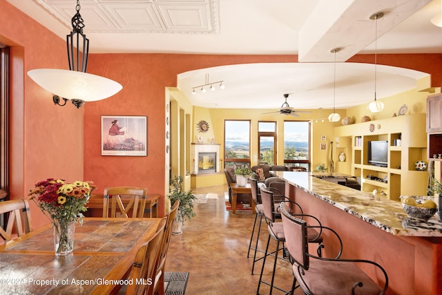 kitchen with a kitchen bar, light stone counters, ceiling fan, concrete floors, and hanging light fixtures