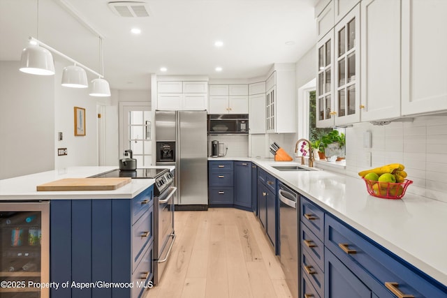 kitchen with a sink, stainless steel appliances, light wood-style flooring, blue cabinets, and beverage cooler