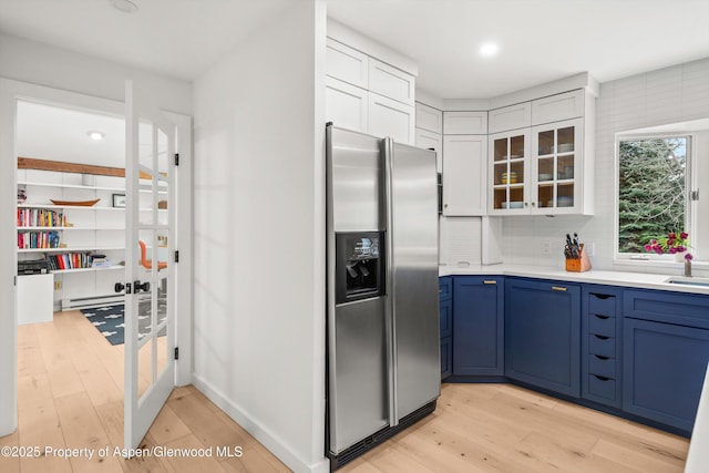 kitchen with light wood-style flooring, glass insert cabinets, blue cabinets, light countertops, and stainless steel fridge