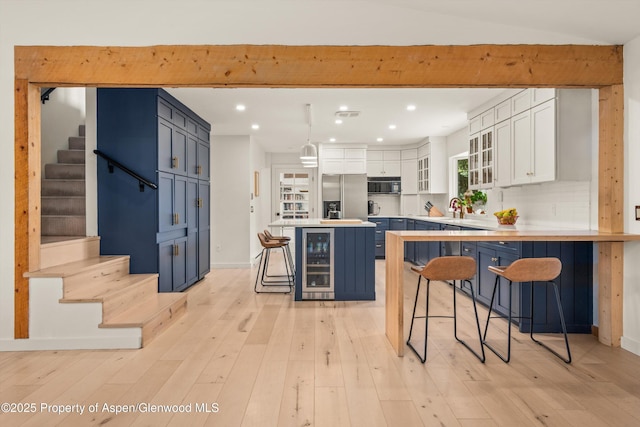 kitchen with a kitchen breakfast bar, black microwave, beverage cooler, blue cabinetry, and stainless steel refrigerator with ice dispenser