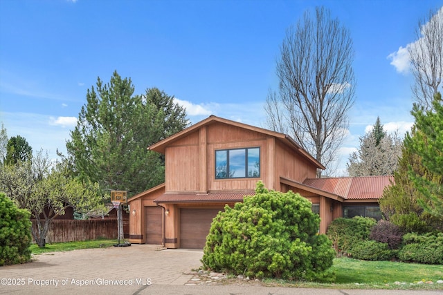 view of front of property featuring fence, driveway, metal roof, and a garage