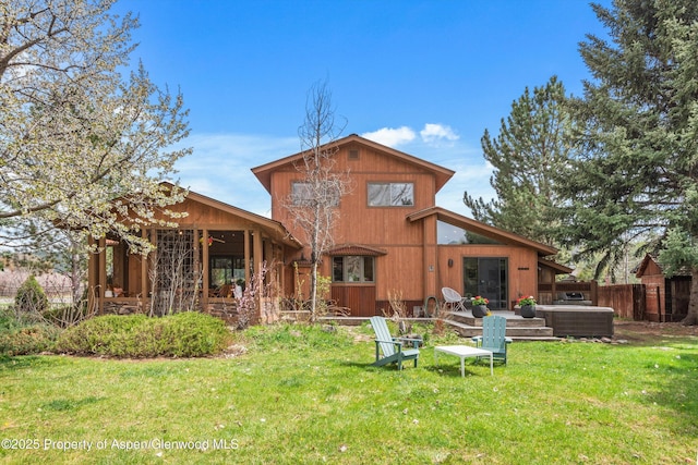 rear view of property featuring a lawn, fence, and a hot tub