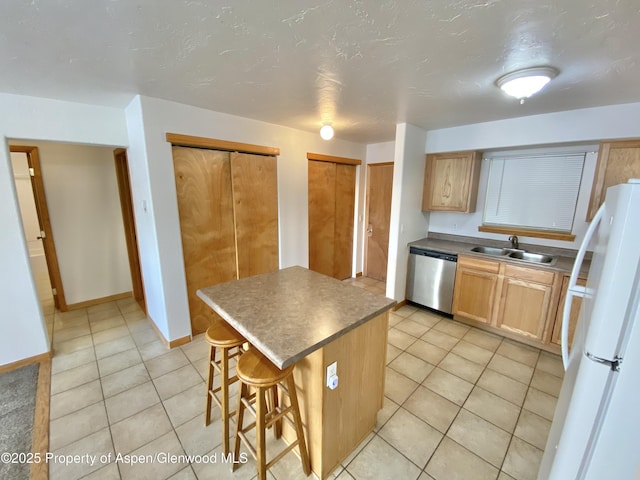 kitchen with sink, stainless steel dishwasher, white fridge, a breakfast bar area, and a kitchen island