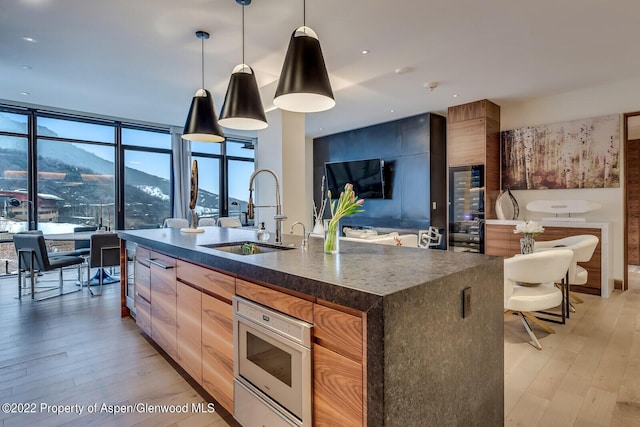 kitchen featuring pendant lighting, floor to ceiling windows, sink, light wood-type flooring, and an island with sink