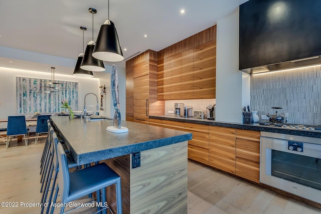 kitchen featuring a kitchen island with sink, sink, hanging light fixtures, appliances with stainless steel finishes, and a kitchen bar