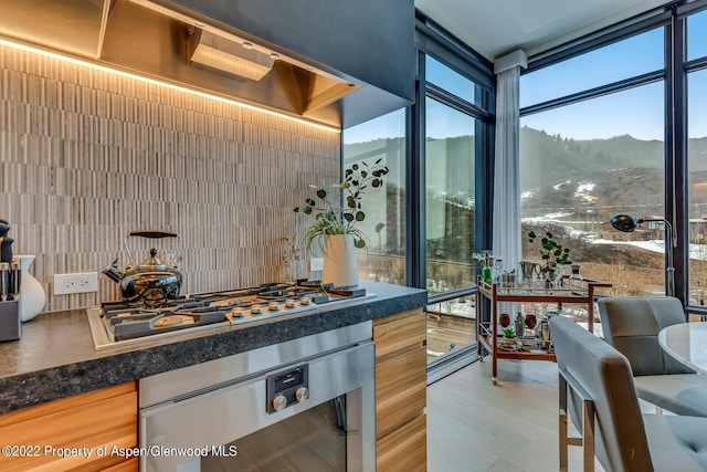 kitchen featuring a mountain view, stainless steel gas stovetop, light wood-type flooring, wall oven, and a wall of windows