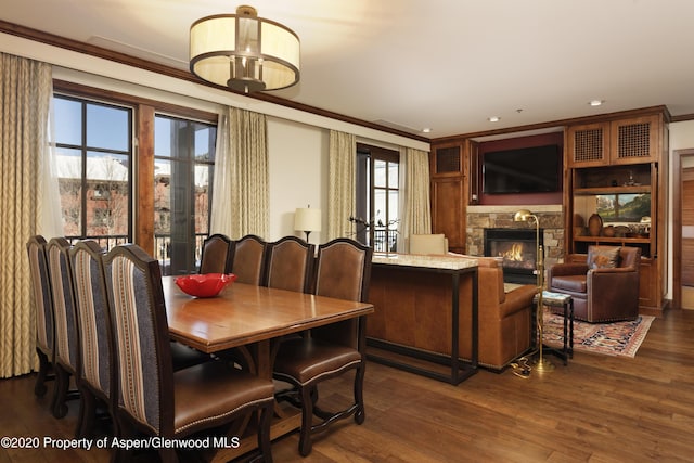 dining space with a fireplace, a healthy amount of sunlight, crown molding, and dark wood-type flooring