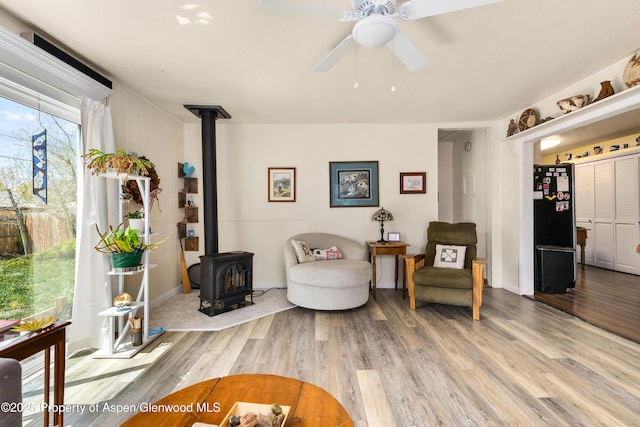 sitting room featuring a wood stove, light wood-style flooring, and a ceiling fan
