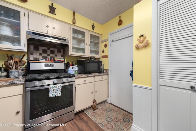 kitchen featuring gas stove, black microwave, glass insert cabinets, dark wood-style flooring, and under cabinet range hood