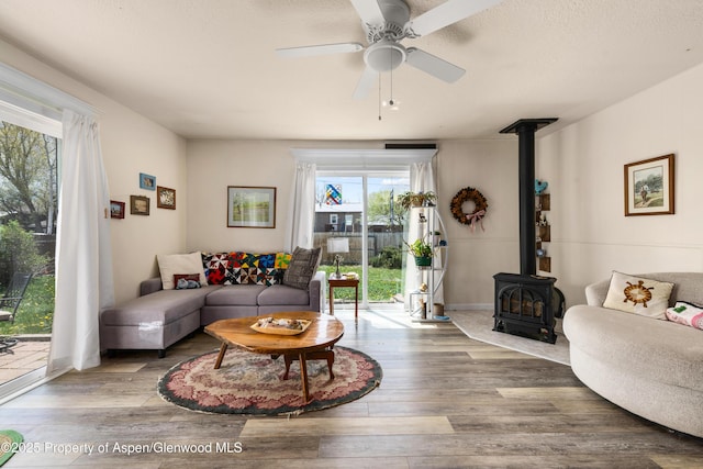 living room featuring a wood stove, ceiling fan, and wood finished floors