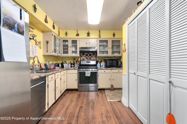 kitchen with stainless steel appliances, a sink, a textured ceiling, dark wood-type flooring, and light countertops