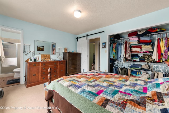 carpeted bedroom with a barn door, a closet, connected bathroom, and a textured ceiling