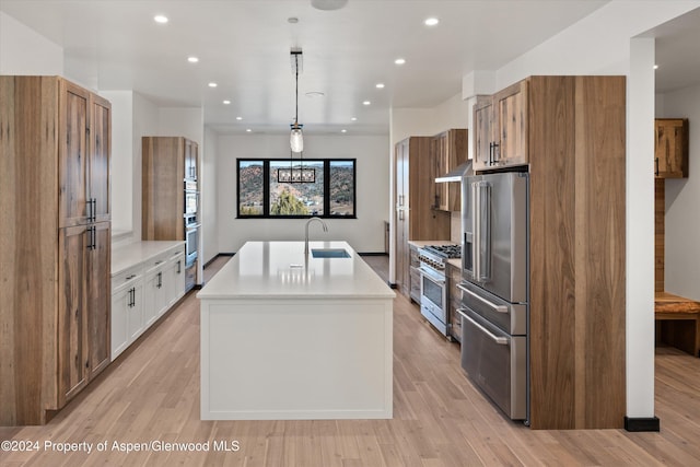 kitchen featuring high end appliances, white cabinets, a center island with sink, sink, and hanging light fixtures