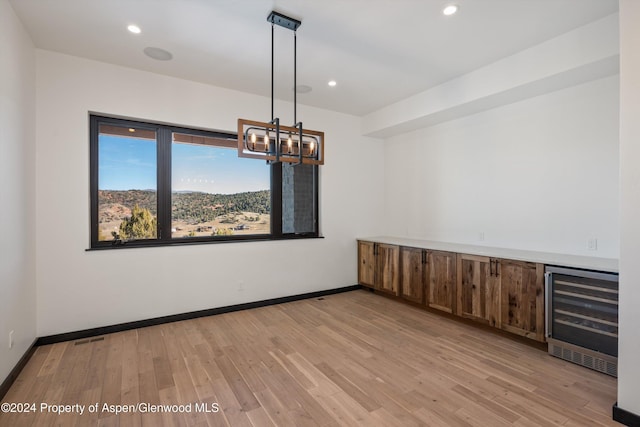 unfurnished room with wine cooler, a chandelier, and light hardwood / wood-style floors