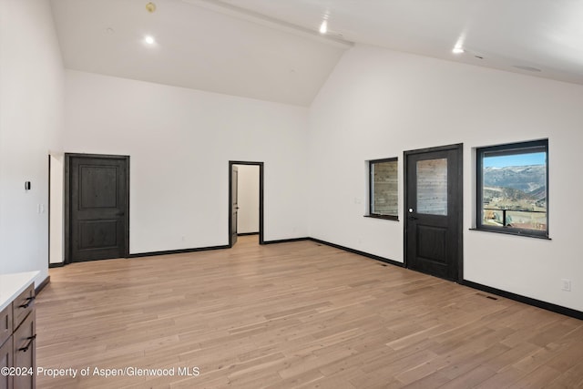 unfurnished room featuring light hardwood / wood-style floors, beam ceiling, and high vaulted ceiling