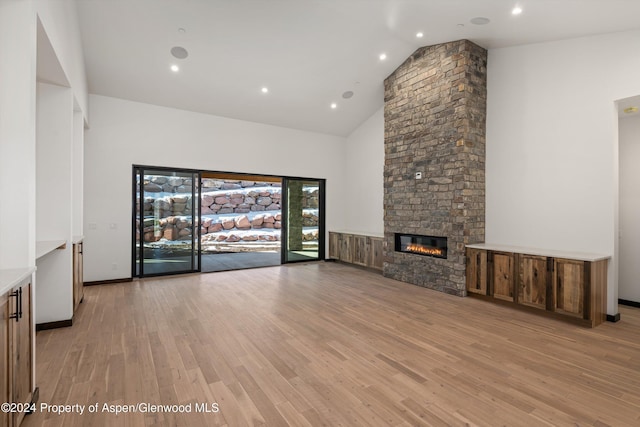 unfurnished living room with a fireplace, light wood-type flooring, and high vaulted ceiling