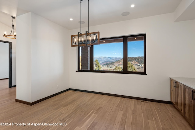 unfurnished dining area featuring light wood-type flooring and an inviting chandelier