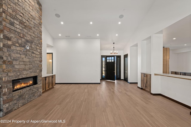 unfurnished living room with a fireplace, a high ceiling, light hardwood / wood-style floors, and a notable chandelier