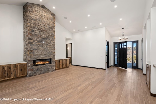 unfurnished living room featuring light hardwood / wood-style flooring, high vaulted ceiling, a chandelier, and a brick fireplace