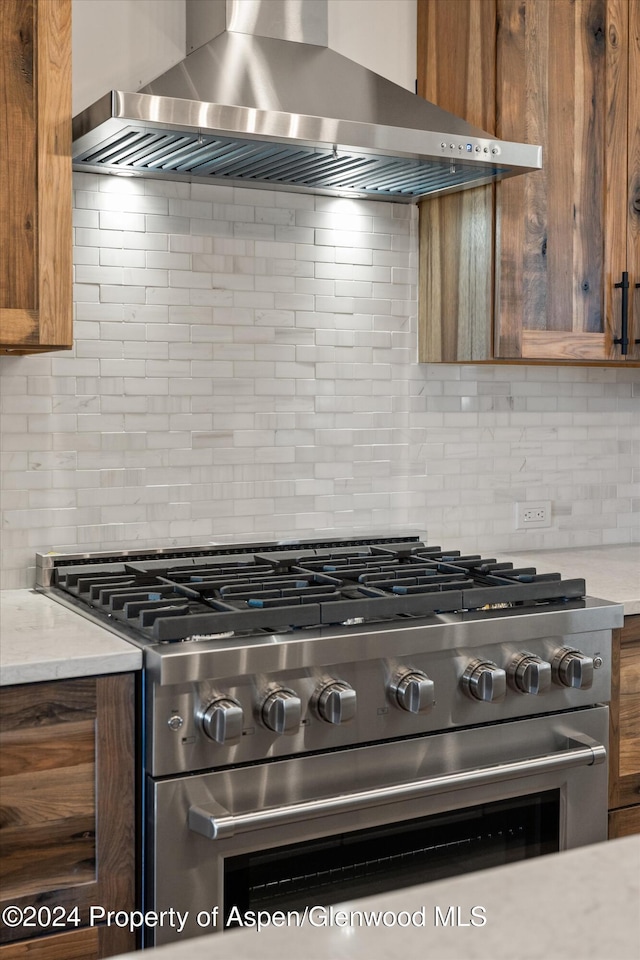 kitchen featuring high end range, tasteful backsplash, and wall chimney range hood