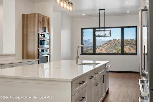 kitchen with pendant lighting, a kitchen island with sink, sink, appliances with stainless steel finishes, and white cabinetry