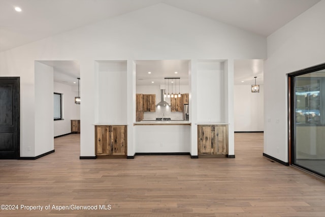 kitchen with wall chimney range hood, high vaulted ceiling, and light hardwood / wood-style flooring