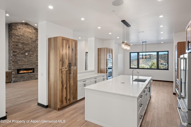 kitchen featuring stainless steel appliances, a kitchen island with sink, sink, a fireplace, and white cabinetry