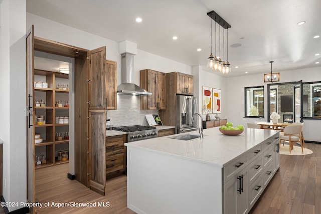 kitchen featuring white cabinets, a center island with sink, wall chimney range hood, sink, and decorative light fixtures