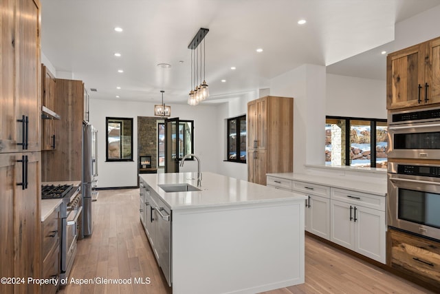 kitchen with stainless steel appliances, sink, pendant lighting, a center island with sink, and white cabinetry