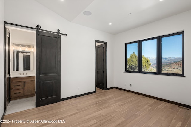 unfurnished bedroom featuring sink, a barn door, ensuite bathroom, light hardwood / wood-style floors, and lofted ceiling