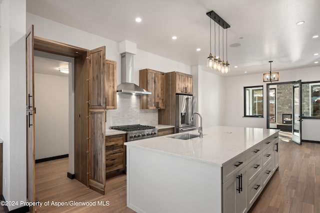 kitchen with pendant lighting, a kitchen island with sink, white cabinets, wall chimney range hood, and sink