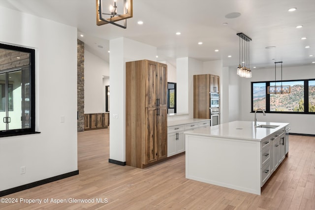 kitchen with sink, decorative light fixtures, white cabinets, light hardwood / wood-style floors, and an island with sink