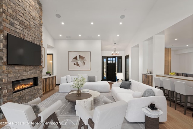 living room with a chandelier, vaulted ceiling, light hardwood / wood-style floors, and a stone fireplace