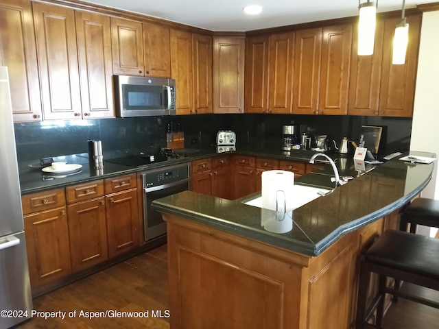 kitchen featuring appliances with stainless steel finishes, tasteful backsplash, dark wood-type flooring, hanging light fixtures, and a breakfast bar area