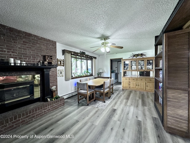 dining area featuring a fireplace, a textured ceiling, light wood-type flooring, and a baseboard radiator