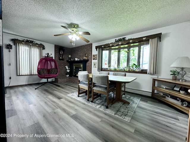 dining space with light wood-type flooring, a textured ceiling, baseboard heating, ceiling fan, and a fireplace