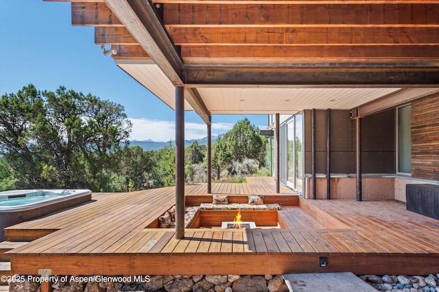 deck with an outdoor fire pit and an outdoor hot tub