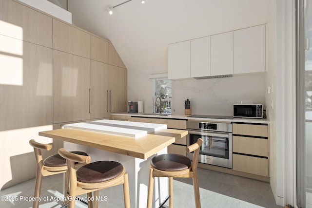 211 W Main St, Aspen, CO 81611 - kitchen featuring oven, a sink, modern cabinets, a breakfast bar area, and vaulted ceiling