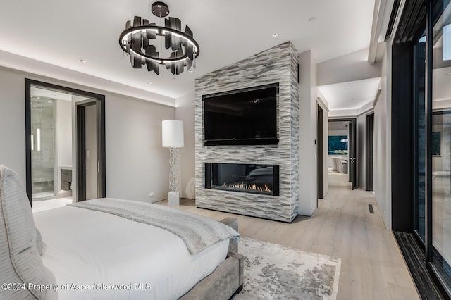 bedroom with a fireplace, connected bathroom, light hardwood / wood-style floors, and a chandelier