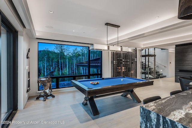 recreation room with a raised ceiling, a wall of windows, pool table, and light hardwood / wood-style flooring