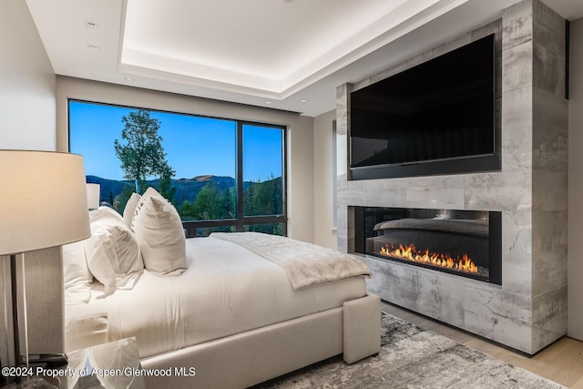 bedroom with a raised ceiling, a large fireplace, and light hardwood / wood-style floors