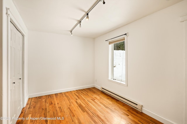 empty room with a baseboard heating unit, rail lighting, light wood-style flooring, and baseboards