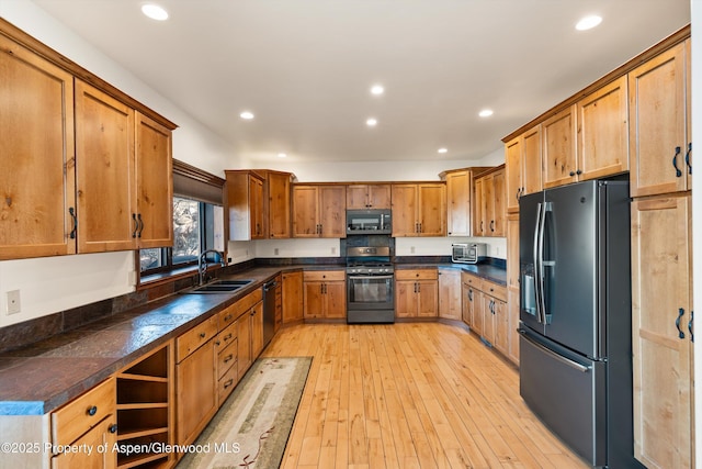 kitchen with light wood-type flooring, a sink, stainless steel appliances, dark countertops, and brown cabinets