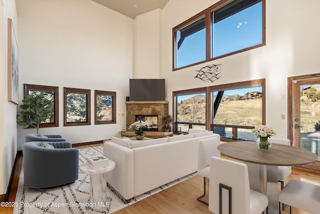 living room featuring light wood-type flooring, a high ceiling, and a stone fireplace