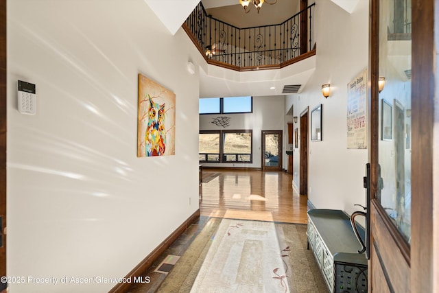 hallway featuring visible vents, baseboards, a high ceiling, and wood finished floors