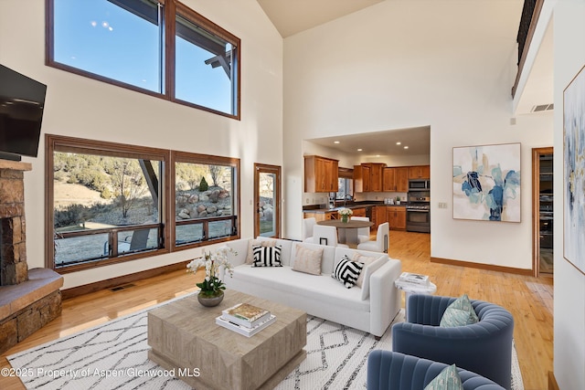 living room featuring visible vents, baseboards, recessed lighting, a stone fireplace, and light wood-style floors