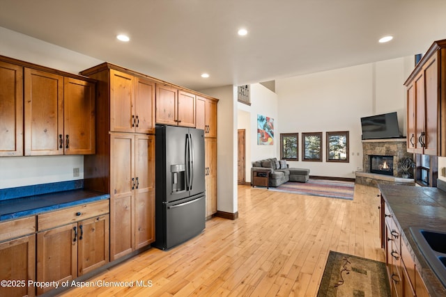 kitchen featuring dark countertops, open floor plan, refrigerator with ice dispenser, light wood-style flooring, and a fireplace